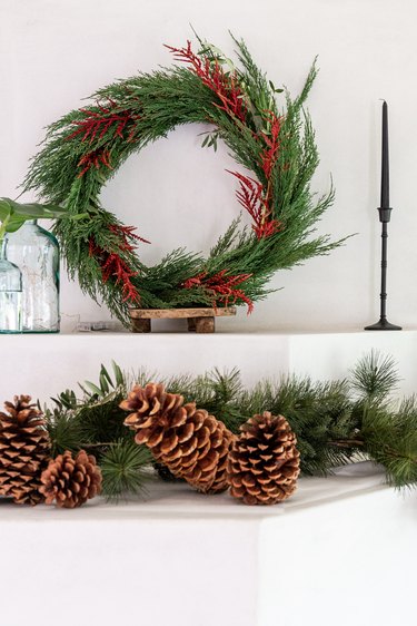 christmas wreath with garland and pinecones on mantel next to black taper candlesticks