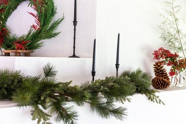 christmas garland on mantel styled with black candlesticks and pinecones