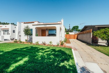 A front lawn of a Spanish style white house with terra-cotta roof tiles