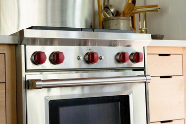 An oven with red knobs. Light wood cabinets, a white counter, and a container of wood utensils.