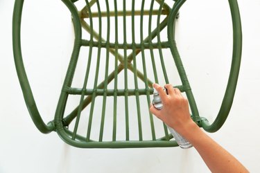 Hand with green spray paint can and rattan chair