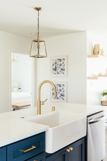 Gold faucet sink in a kitchen island with dark blue cabinets and white countertop. Gold lantern pendant light.