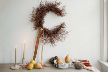 Grapevine and dried Plumosus fern crescent moon wreath with a neutral satin ribbon, with pears, dishes, and pine cones