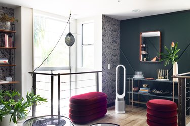 Air purifier in green walled room with red ottomans and minimalist furniture