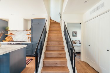 Stairway with wood floor and black rails next to kitchen with blue cabinets and marble countertops