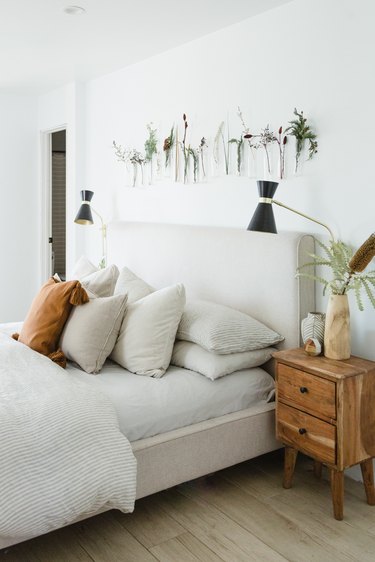 beige upholstered headboard with white bedding and plat hangings on wall