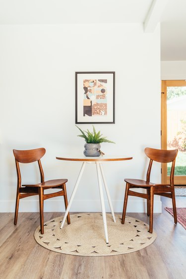 Two wood chairs on a wood floor with a round rug and on either side of a round white dining table with an aloe plant and framed wall art