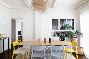 Wood dining table with yellow and white chairs and a contemporary chandelier