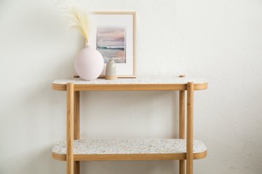 Wood IKEA Listerby console table with terrazzo-inspired wallpaper, round pink vase of pampas grass, and art
