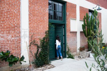 Woman walking through green door of brick building