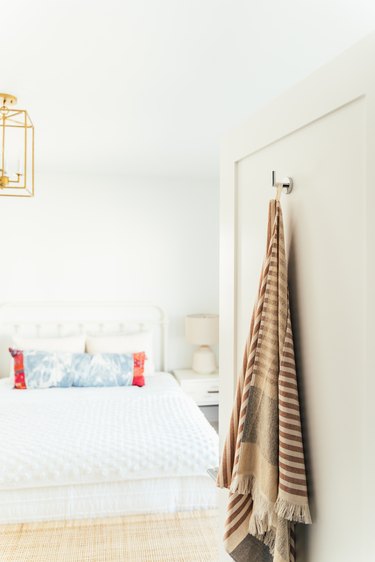 A shawl or a blanket hanging on a door leading to a bedroom with a gold lantern ceiling light and bedding with colorful pillows
