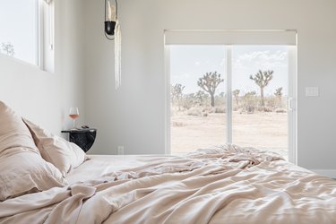 Minimalist bedroom with beige bedding, black accents, and a window with trees of a desert