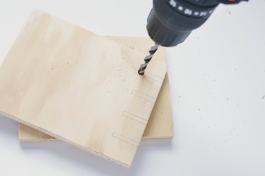 holes being drilled into a square of plywood