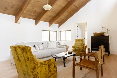 Living room with eclectic furniture, art deco pendant light, and a slanted wood beam ceiling.