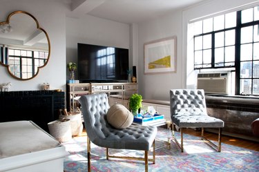 Two mid-century gray upholstered chairs sit on a colorful pastel rug in the living room.