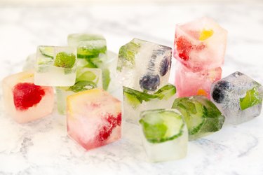 Ice cubes with mint, rosemary, raspberries, strawberries, blueberries, lemon peel, and cucumber