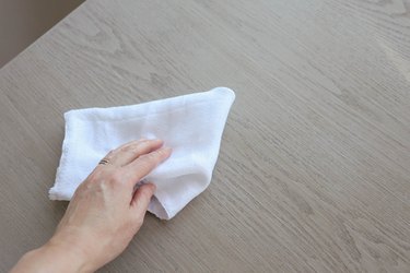 Person using a drop cloth to clean a wood tabletop with household surface cleaner or degreaser