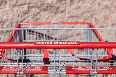 A red Costco shopping cart in front of a light red brick wall.