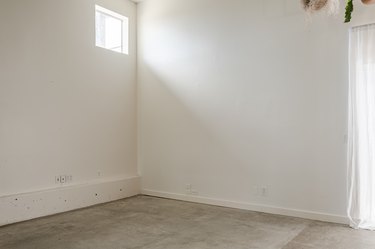 an empty white-walled room with a small, square window in the corner
