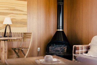 A wood-burning stove in the corner of a room with retro wood paneling.