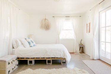 a bed with a frame made out of wood and cinder blocks, with vintage suitcases as a bedside table