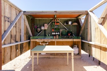 a small outdoor kitchen with wall-mounted racks for cups and plates and pots hanging from a rod