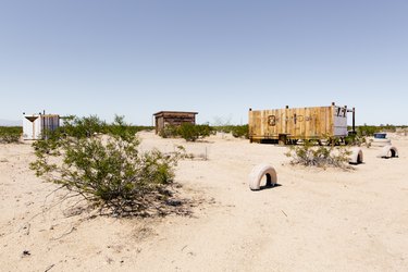 a view across scrubby desert of three rustic wooden buildings