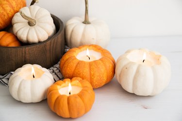 Lit orange and white pumpkin candles, a wood bowl with pumpkins