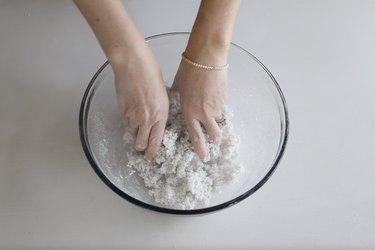 A person using their hands to mix paper mache pulp and water in a bowl