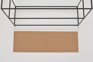 Carboard panel laying next to black metal shelving frame against a white background