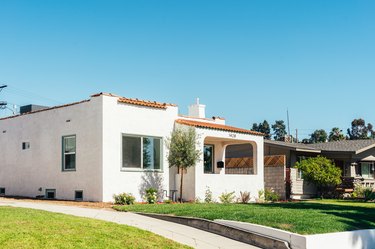 A front lawn and driveway of a Spanish style white house with terra-cotta roof tiles