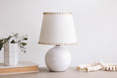 IKEA SKOTTORP lampshade with leather whipstitching, on a table with a book, and a vase of flowers