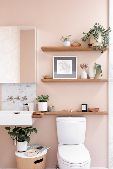 eco-friendly bathroom idea for pink bath with three wooden floating shelves above a toilet