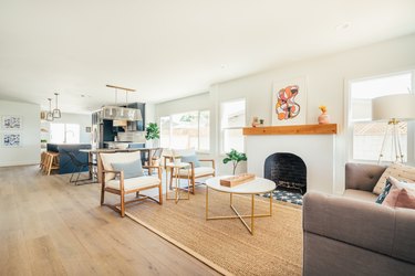 Living room with wood mantel fireplace, round coffee table, wood armchairs with blue pillows, and wood flooring.