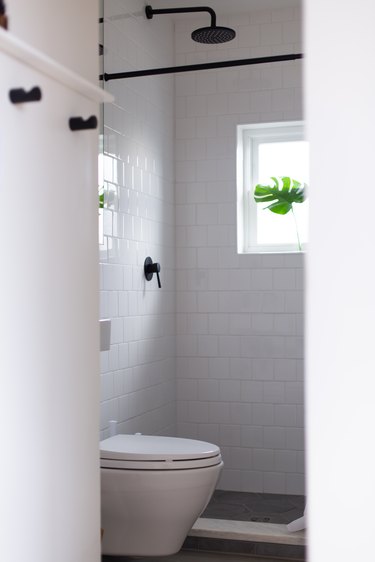 White subway tile bathroom with white toilet and shower window  with monstera leaf