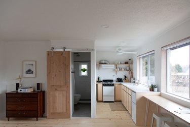 Full studio view with dresser and record player, barn door and bathroom, galley kitchen with open shelving