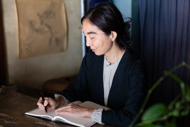 Woman writing in book at wooden desk against blue multipaneled wall