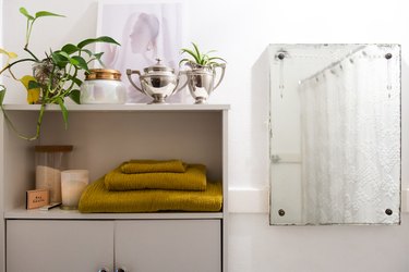 A mirror next to a white cabinet with yellow towels and houseplants.