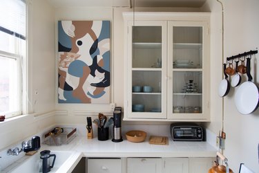 White kitchen counter with windowed shelving unit and pots and pans hanging over stove