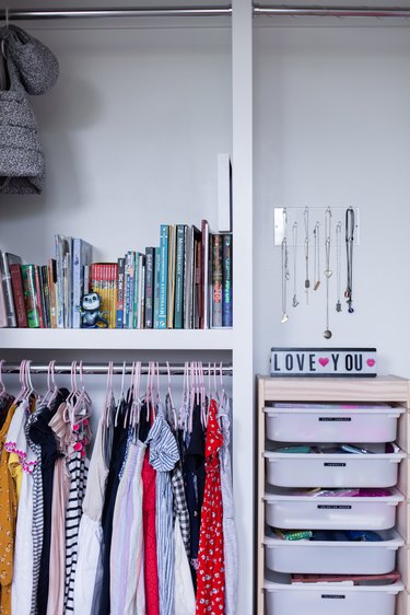Closet with kid's clothes, children's books, plaster drawer containers, and a wall jewelry holder.