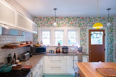Kitchen with flower wallpaper and retro accents. Yellow pendant light over a wood table, and light blue floor.
