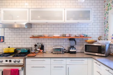 a kitchen counter with a toaster, blender, and microwave and a white subway tile backsplash
