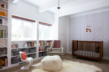 Baby's room with a wood crib, fur rug, globe pendant light, modernist accent chairs, and built-in bookcases.