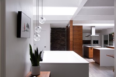 Contemporary Minimalist kitchen with globe pendant lights, and white counters with wood cabinets.