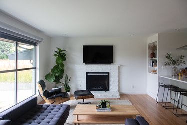 Minimalist living room with modernist furniture, plants, and a tv on top of a white brick fireplace.
