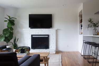 Minimalist living room with modernist furniture, plants, and a tv on top of a white brick fireplace.
