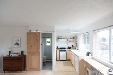 Full studio view with white walls, dresser, barn bathroom door, galley kitchen with open shelving