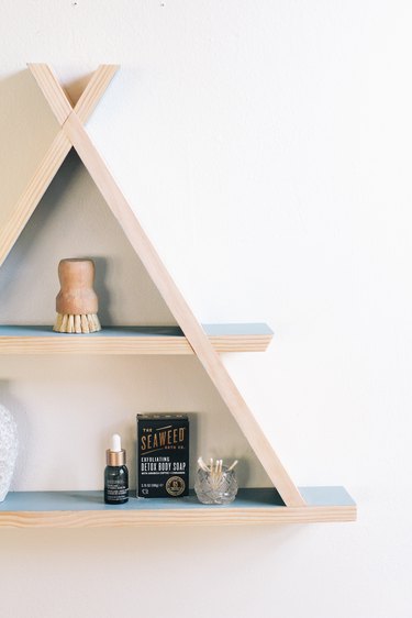 Wooden a-frame shelf with blue inner walls holding small containers on white wall