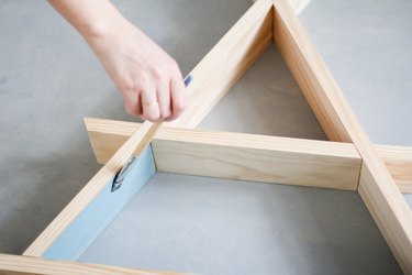 Hand painting inner walls of wooden a-frame shelf against grey background