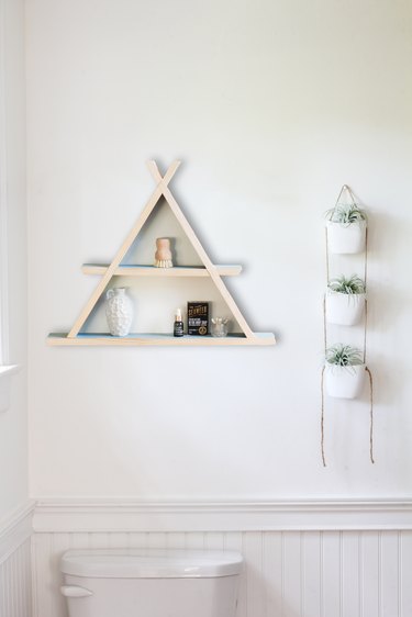 Wooden a-frame shelf holding small containers on white wall next to hanging succulent wall-holder